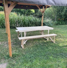 Vue d’ensemble d’un mobilier artisanal composé d’une table et de deux bancs, installé sous une tonnelle en bois. Un espace accueillant pour les repas d’été.