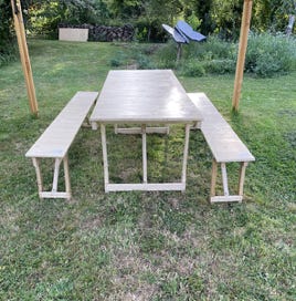 Ensemble de table et bancs pliants vus de côté. Bois massif, finitions soignées et lignes harmonieuses pour sublimer les moments partagés.