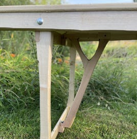 Zoom sur le pied en frêne et le mécanisme de tréteaux pliants intégrés. Un système inspiré des anciennes tables de ferme pour une installation rapide et pratique.